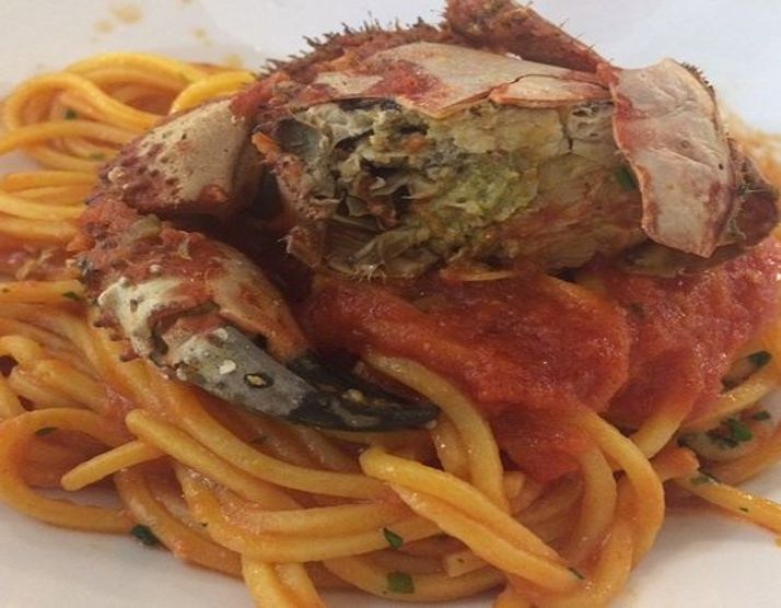 Un piatto di pasta al sugo di pelosi: il granchio, cucinato intero, è adagiato sulla pasta con il sugo di pomodoro e il prezzemolo